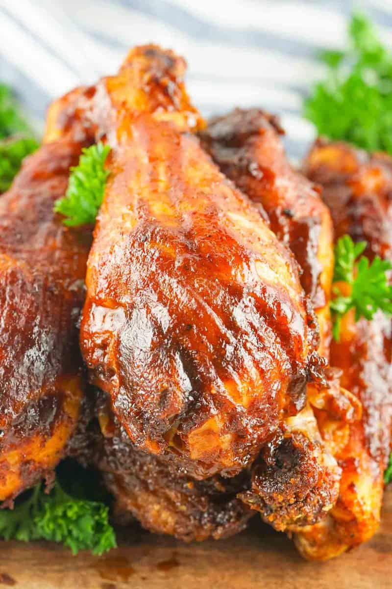 smoked chicken drumsticks stacked on a wood board.