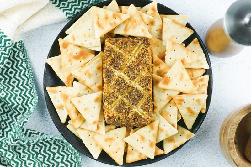 smoked cream cheese with pizza seasoning and crackers on a round platter.
