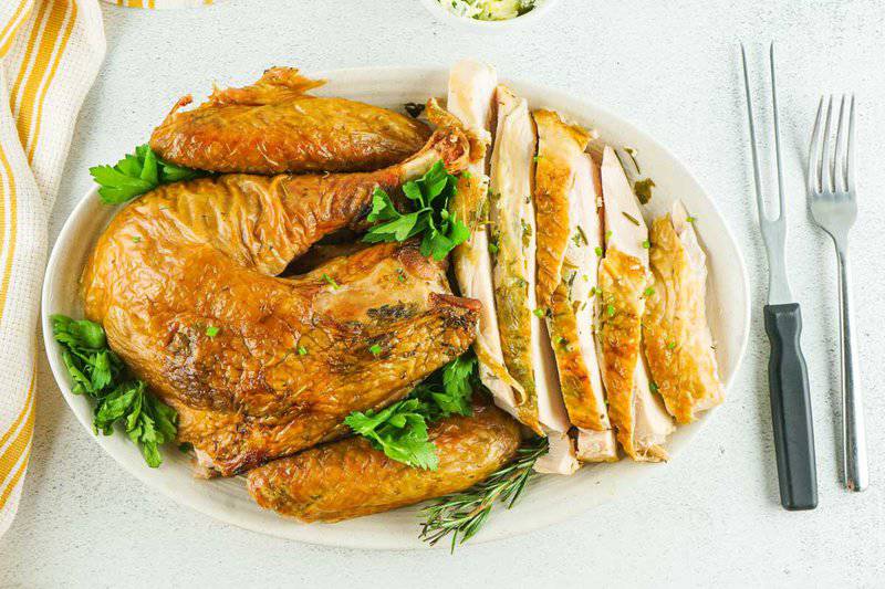 smoked spatchcock turkey pieces and slices on a white platter.