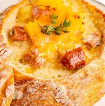 sausage stew topped with cheddar cheese in a bread bowl.
