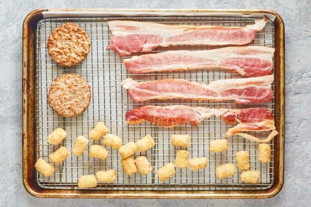 bacon, sausage patties, and hash browns on a wire rack over a baking sheet.