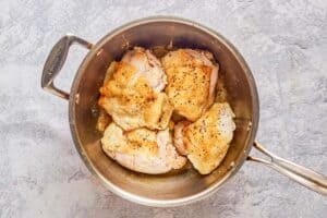 partially cooked chicken thighs in a large pot.