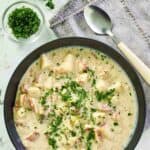 overhead view of a bowl of clam chowder, a spoon, and fresh parsley.