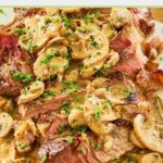 closeup of sliced steak marsala with sauce on a platter.