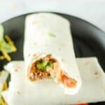 two copycat Taco Bell supreme burritos on a black plate.
