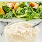 small bowl of creamy caesar salad dressing in front of a salad.