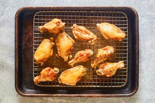 Fried chicken wings draining on a wire rack over a baking sheet.