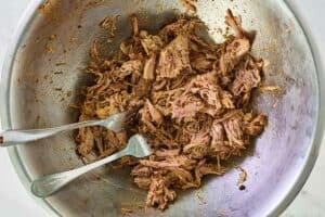 shredded pork shoulder and two forks in a bowl.
