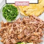 overhead view of pulled pork shoulder, lime wedges, and tortillas on a platter.