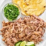 shredded pork shoulder, cilantro, and tortillas on a platter.