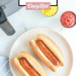 Overhead view of two air fryer hot dogs in buns and cups of ketchup and mustard.