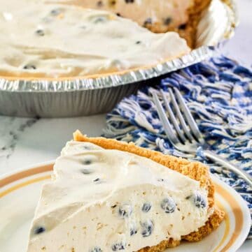 blueberry cream pie slice on a plate and the pie behind it.