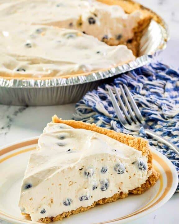 blueberry cream pie slice on a plate and the pie behind it.