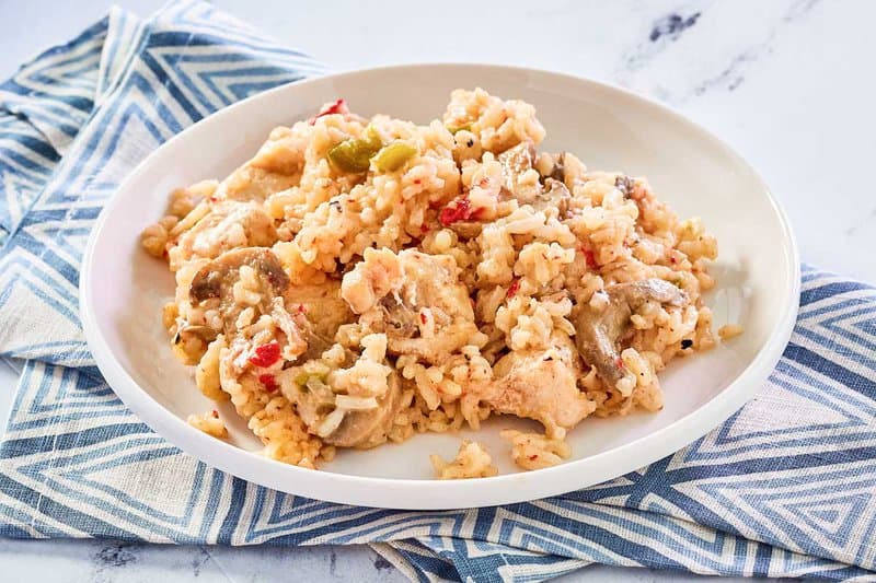 serving of chicken and rice casserole on a white plate on top of a cloth napkin.