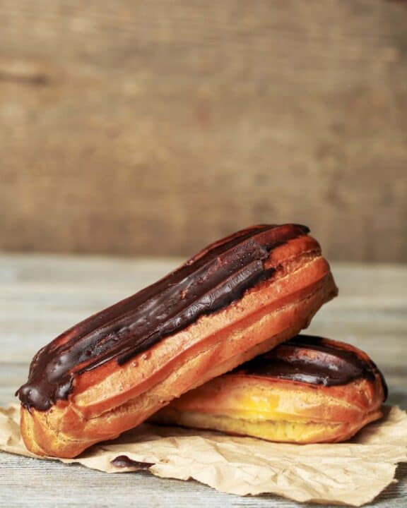 two homemade chocolate eclairs on brown parchment paper.