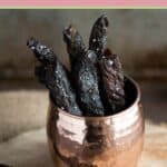Several homemade teriyaki beef jerky strips in a brass cup.