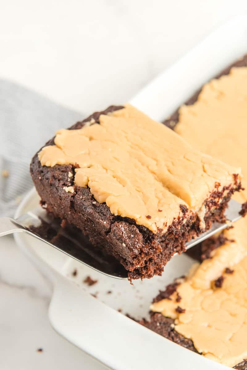 Chocolate caramel cake slice held over the cake.