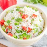 Cilantro rice with bell peppers in a bowl, a red bell pepper, and fresh cilantro.