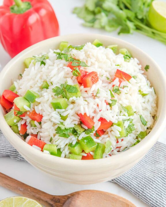 Cilantro rice with bell peppers in a bowl, a red bell pepper, and fresh cilantro.