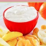 Cool whip fruit dip in a red bowl and fresh fruit in front of it.