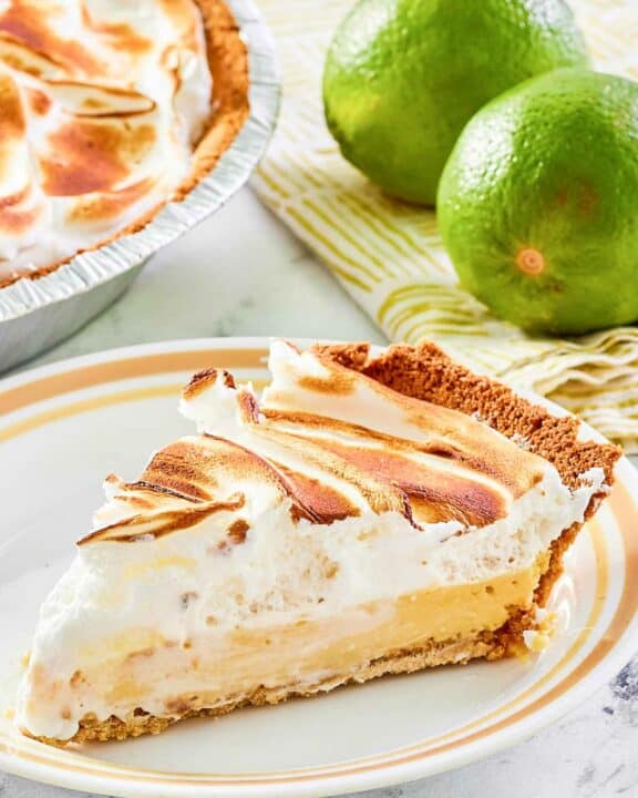 Key lime meringue pie slice on a plate and two limes.