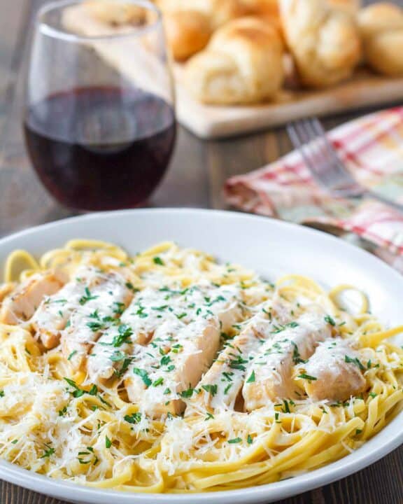 Copycat Olive Garden grilled chicken alfredo, a glass of wine, and bread.