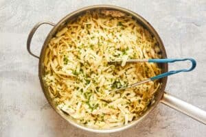 Tossing cooked chicken, alfredo sauce, and pasta in a pot.