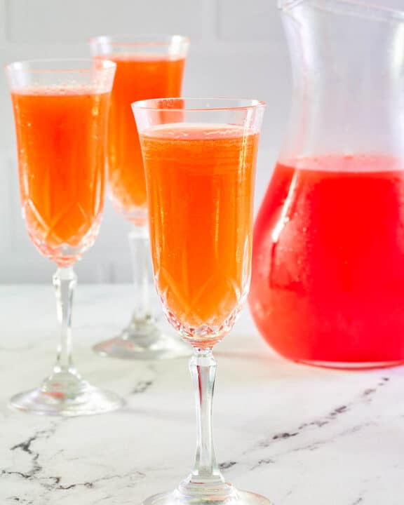 Strawberry mimosa in three glasses and a pitcher.