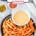 Homemade Taco Bell nacho fries and cheese dipping sauce on a black plate.