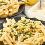 Greek pasta with lemon alfredo sauce on two plates, parmesan cheese, and a lemon.