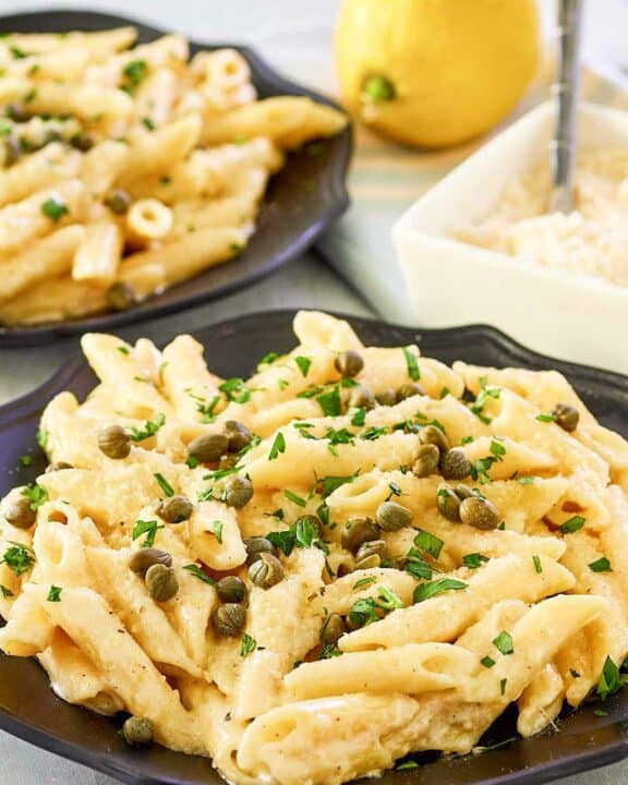 Greek pasta with lemon alfredo sauce on two plates, parmesan cheese, and a lemon.