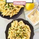 Overhead view of Greek pasta with lemon sauce on plates, a lemon, and parmesan cheese.
