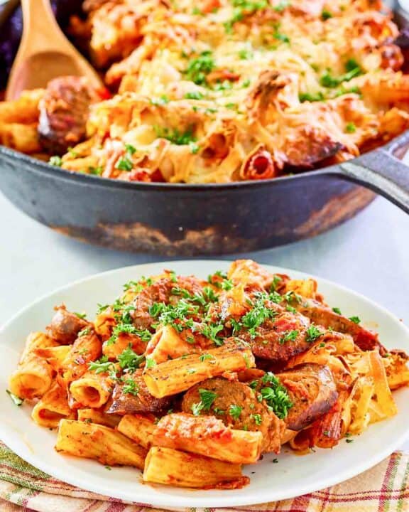 One pot sausage pasta in a skillet and a serving of it on a plate.
