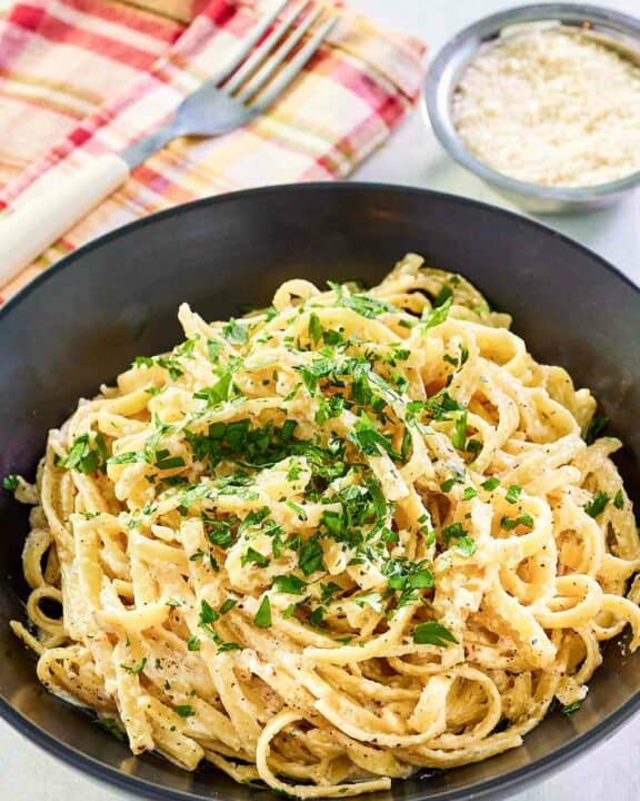 Copycat Pasta House fettuccine alfredo in a large bowl and parmesan cheese in a small bowl.