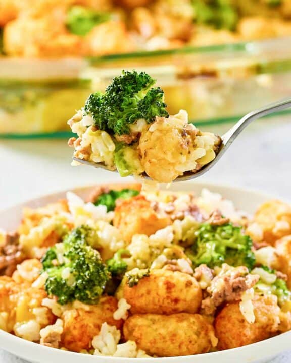 Broccoli tater tot casserole with ground beef on a fork over a plate of it.