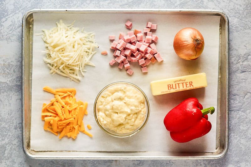 Cheesy hash brown casserole with ham ingredients on a tray.