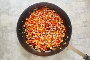 Cooked diced ham, onion, and bell peppers in a skillet.