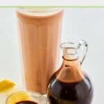 A glass of chocolate milk and homemade chocolate syrup in a glass pitcher.