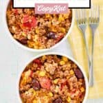 Overhead view of hamburger corn casserole in two bowls and two forks on a yellow napkin.