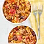 Overhead view of two bowls of hamburger corn casserole and two forks on a napkin.