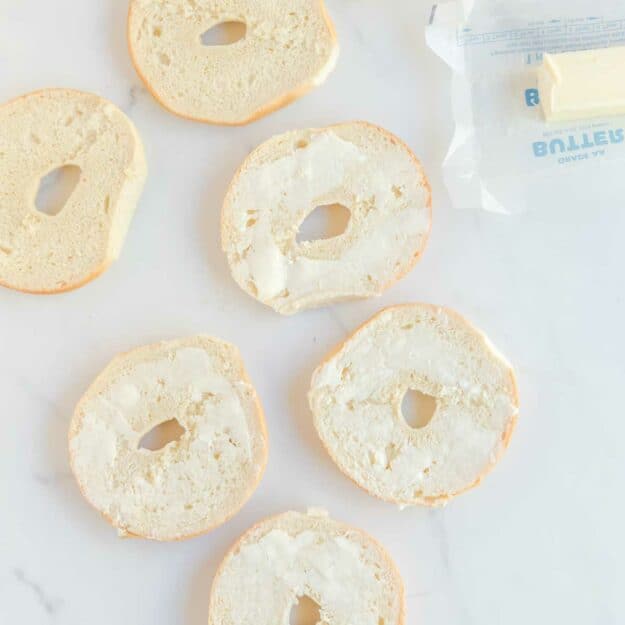 Spreading butter on bagel halves.