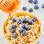 Overnight oats made with milk in a bowl, fresh blueberries, and a bowl of honey.