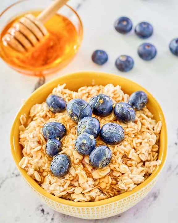 Overnight oats made with milk in a bowl, fresh blueberries, and a bowl of honey.