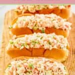 Imitation crab salad in four hoagie rolls on a wood board.