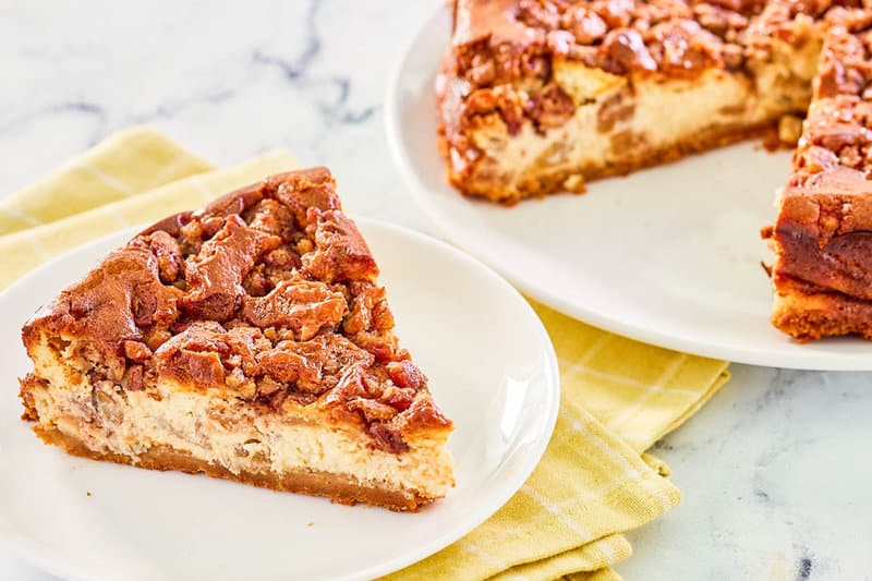 Copycat Olive Garden apple praline cheesecake slice on a plate next to the cheesecake.