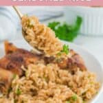 Homemade Texas Roadhouse seasoned rice on a spoon over a plate of it and chicken.