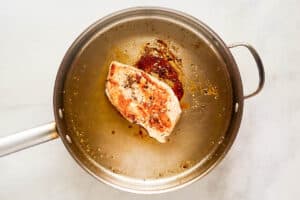 Cooked chicken breast for Thai chicken pizza in a skillet.