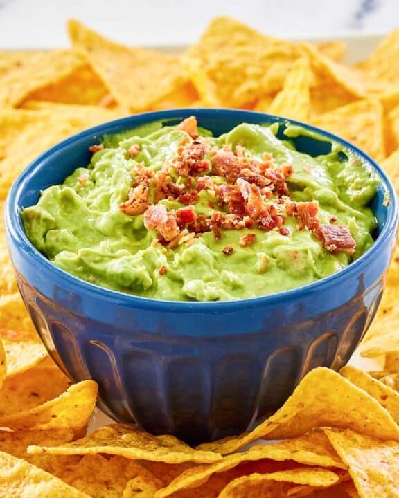 A bowl of avocado dip and tortilla chips on a platter.
