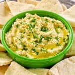 Creamy hummus with yogurt in a green bowl surrounded with pita bread slices.