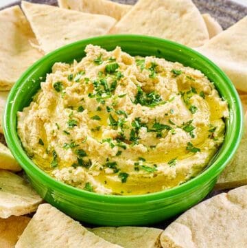 Creamy hummus with yogurt in a green bowl surrounded with pita bread slices.